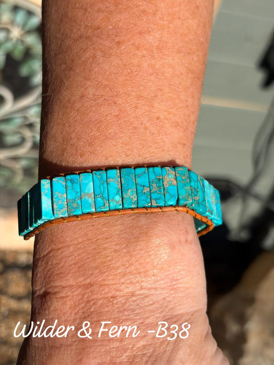 A turquoise beaded bracelet with a brown leather wrap, shown worn on a person's wrist. The text 'Wilder & Fern -B38' is visible in the bottom-left corner By Free Spirit